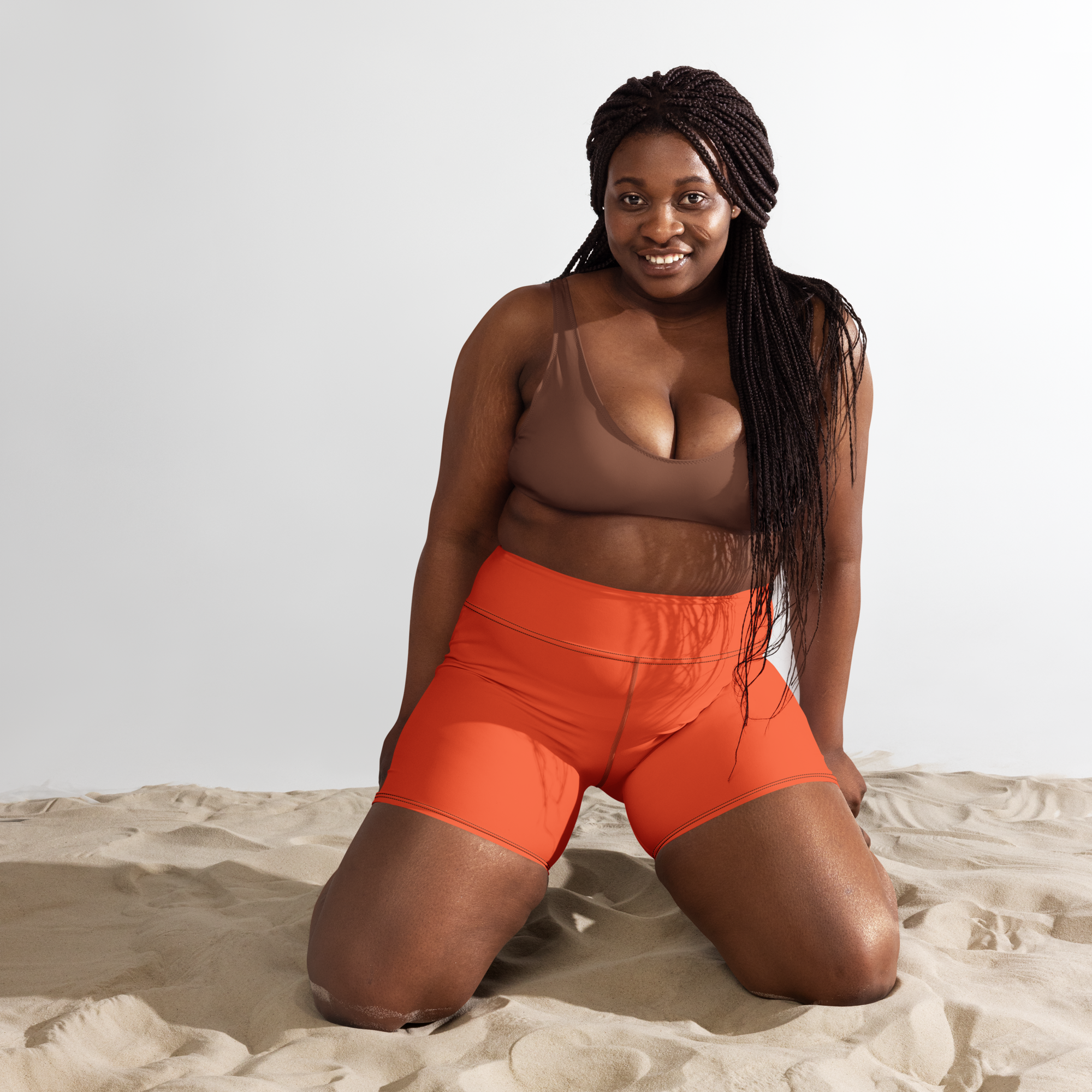 une femme portant un short orange à genoux dans du sable