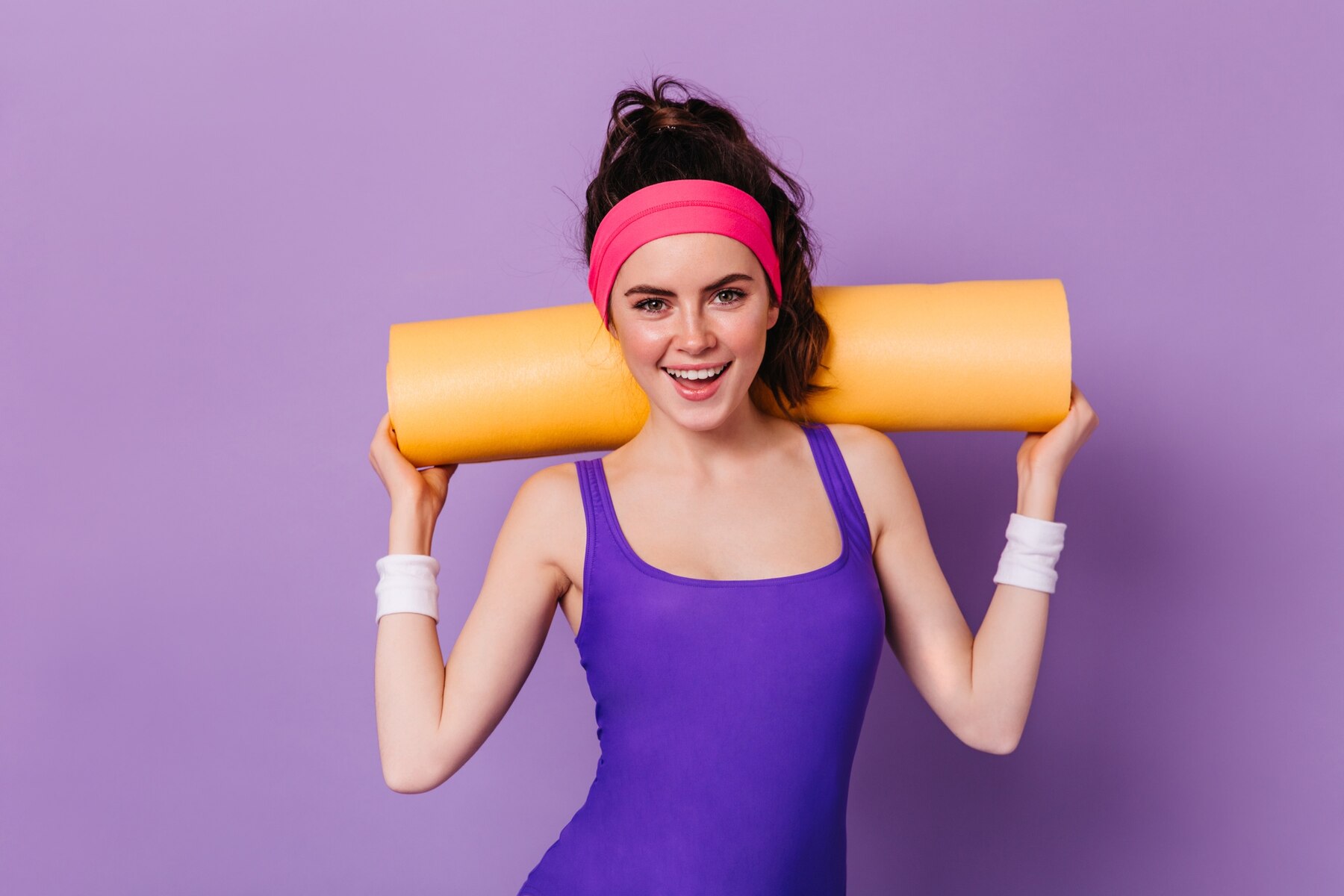 femme souriante tenant un tapis de sport sur ses épaules