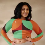 Crop top de sport Hot Focus à manches longues, motif géométrique au couleur vert d'eau, brun, rouge et orange, conçu pour allier confort et style lors des entraînements. Photo porté par le mannequin taille L debout, bras sur les hanches.