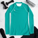 T-shirt manche longue Energy Flow de couleur bleu turquoise en matière lyocell tencel et modal. La photo montre le t-shirt de face dans un décor sportif avec des poids et une gourde pour présenter le produit.